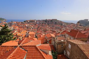 Panoramic view of Dubrovnik's orange terracotta rooftops and historic old town against blue sea.