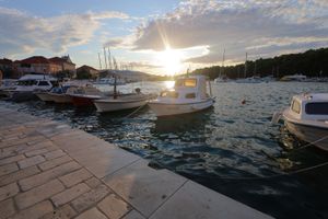 Marina at sunset with boats moored along stone pier under golden sky.