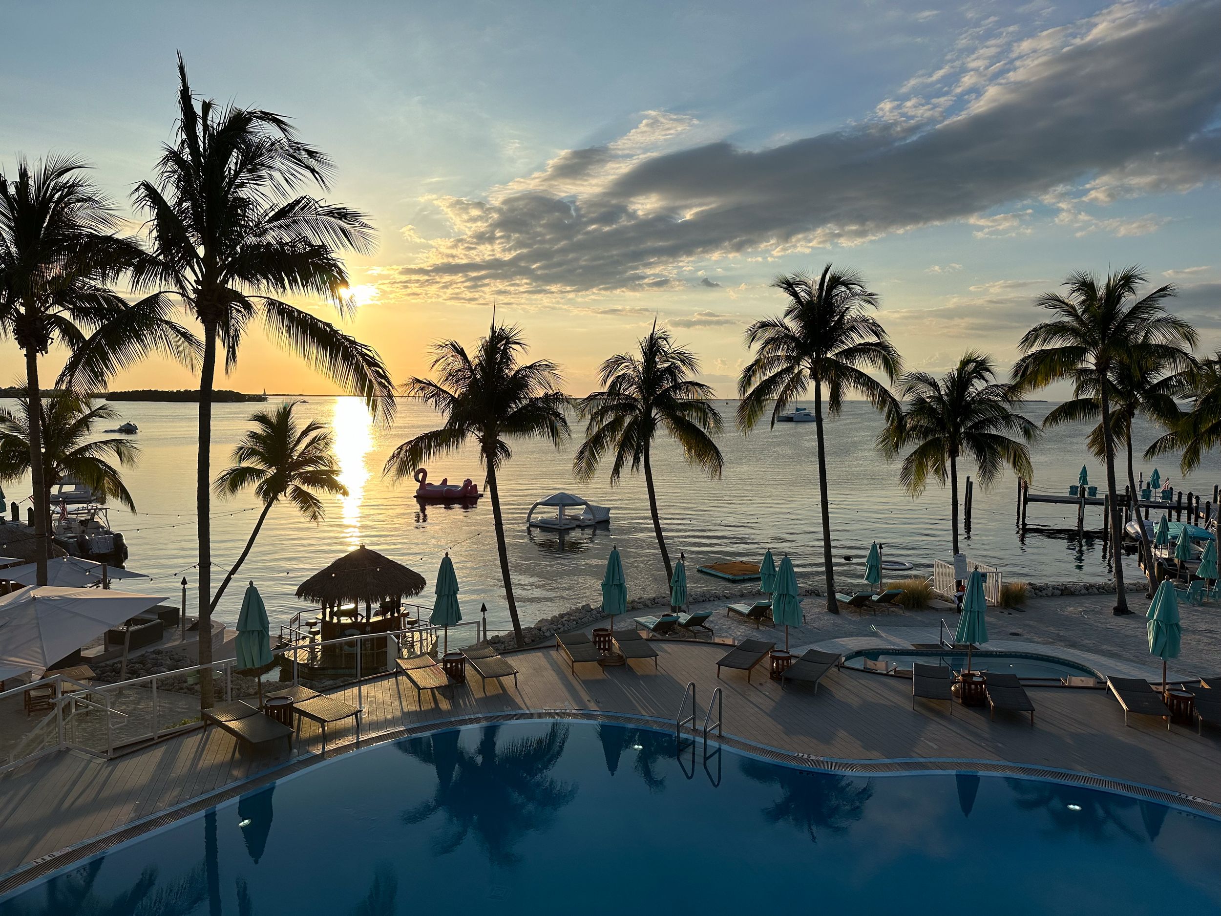 Tropical resort pool deck at sunset with palm trees and ocean view.