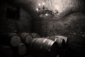 Wine barrels stored in a dark cellar with stone walls and hanging chandelier.