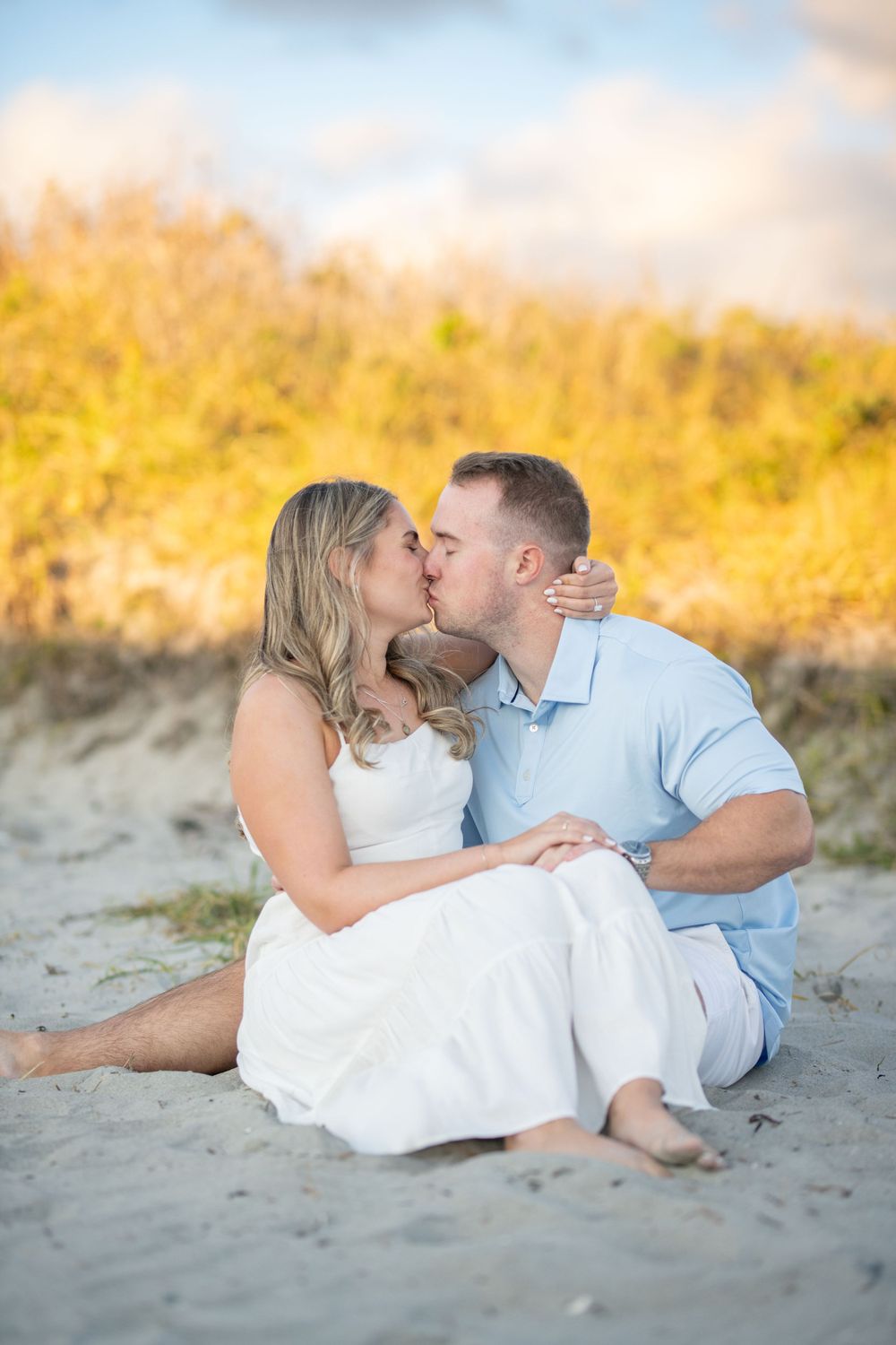 Couple sharing tender moments on sandy beach with warm golden light in background.