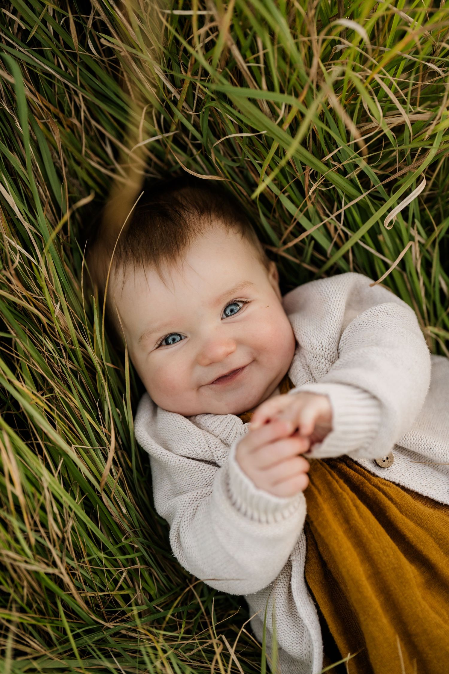 In-home newborn photography in Christchurch – mother cradling baby while sitting on sofa.