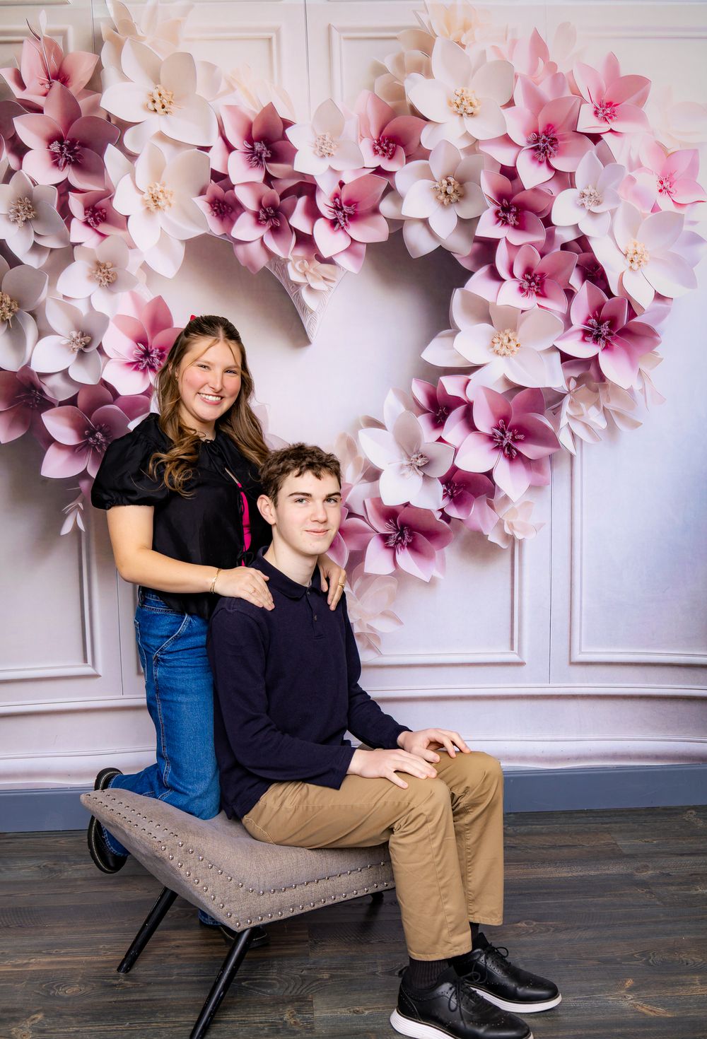 Portrait against elegant pink paper flower backdrop on gray bench.