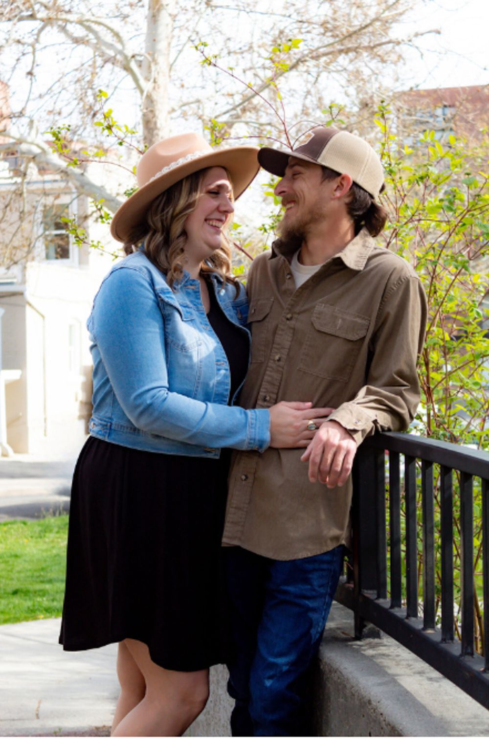 Couple in western wear share an intimate moment on a porch railing during springtime.