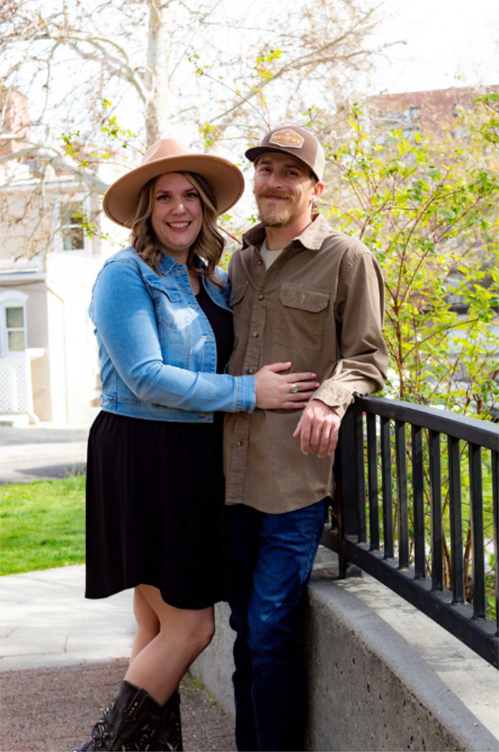 A couple in casual western attire poses together on an outdoor porch during spring.