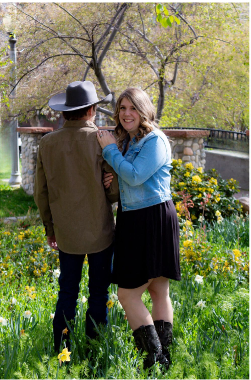 Couple stands together in a garden filled with yellow spring flowers and budding trees.