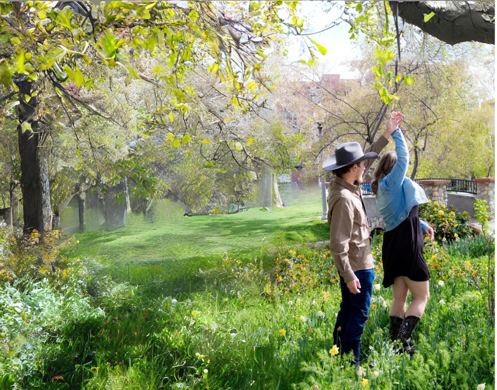 Couple poses playfully in a sunlit spring garden with green grass and trees.