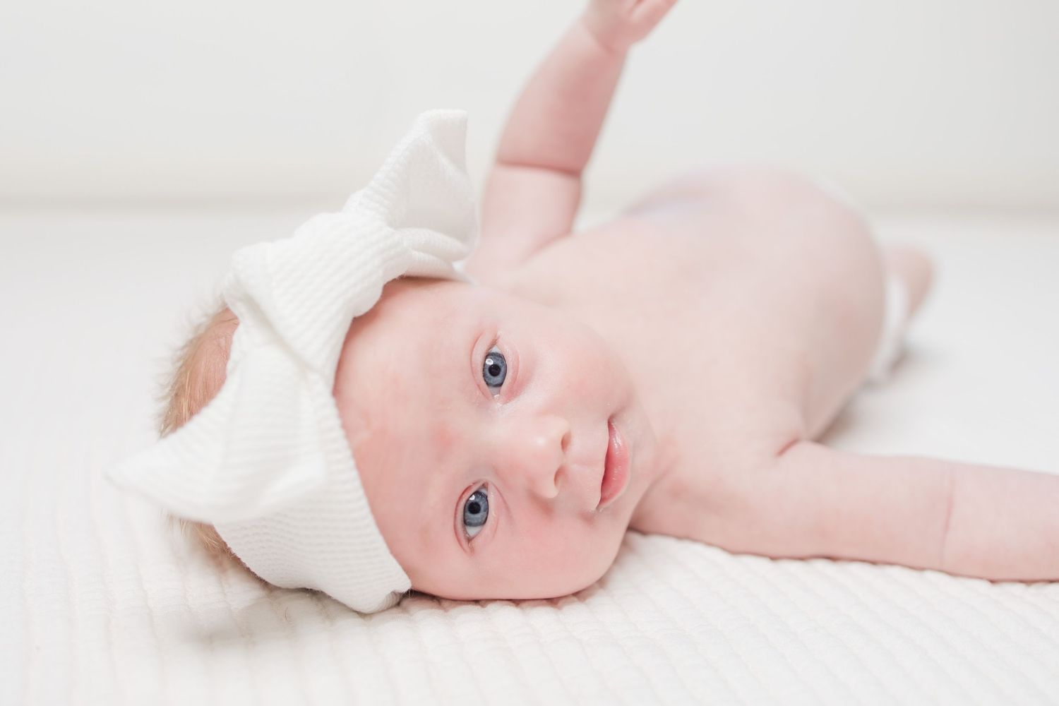 Adorable newborn baby in soft white wrap against a cream background, showcasing delicate innocence.