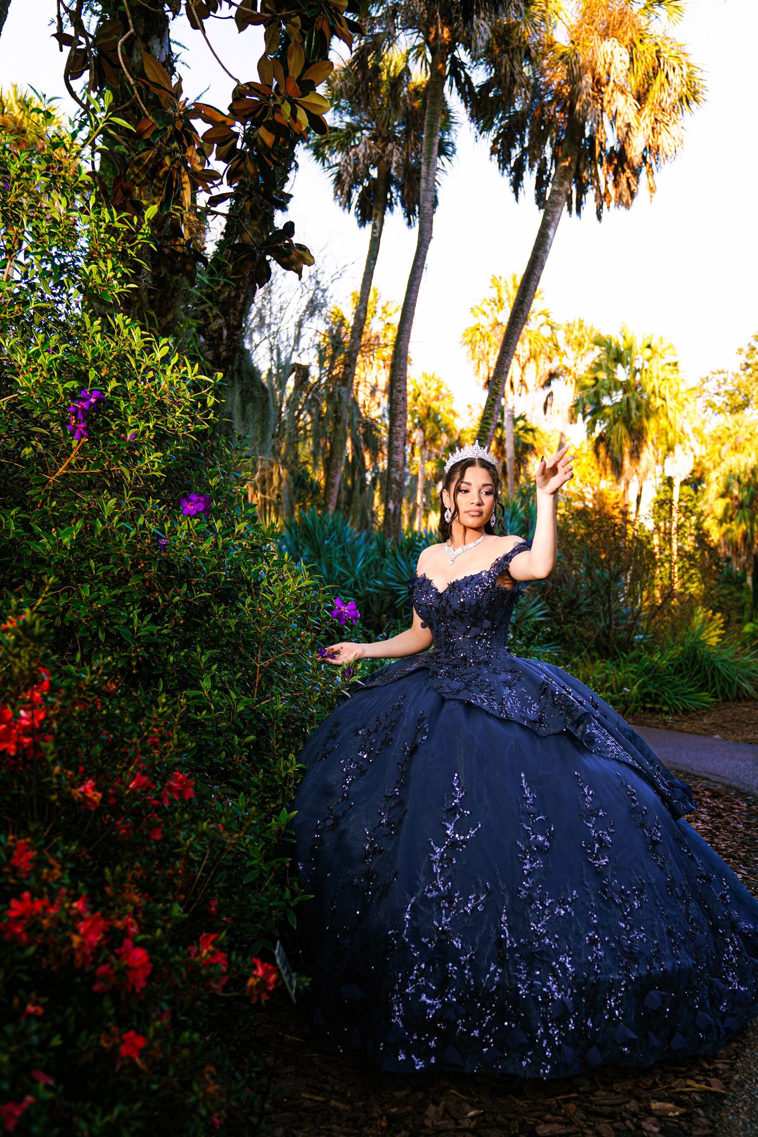 Elegant pink princess ball gown photographed outdoors under green trees in natural sunlight.