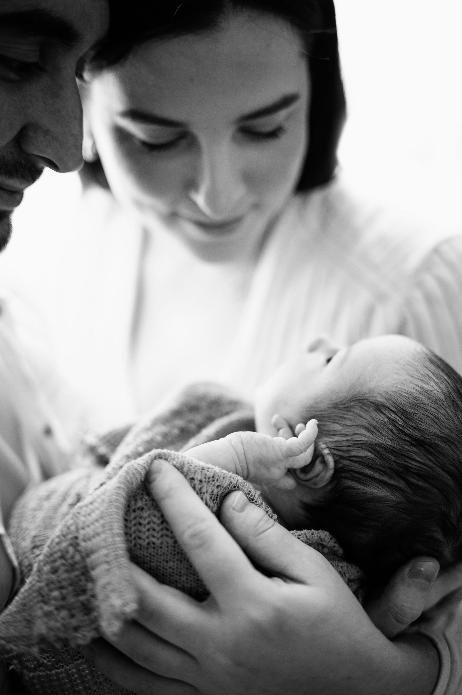 Black and white portrait of tender intimate moment showing a newborn baby being cradled in gentle embrace.