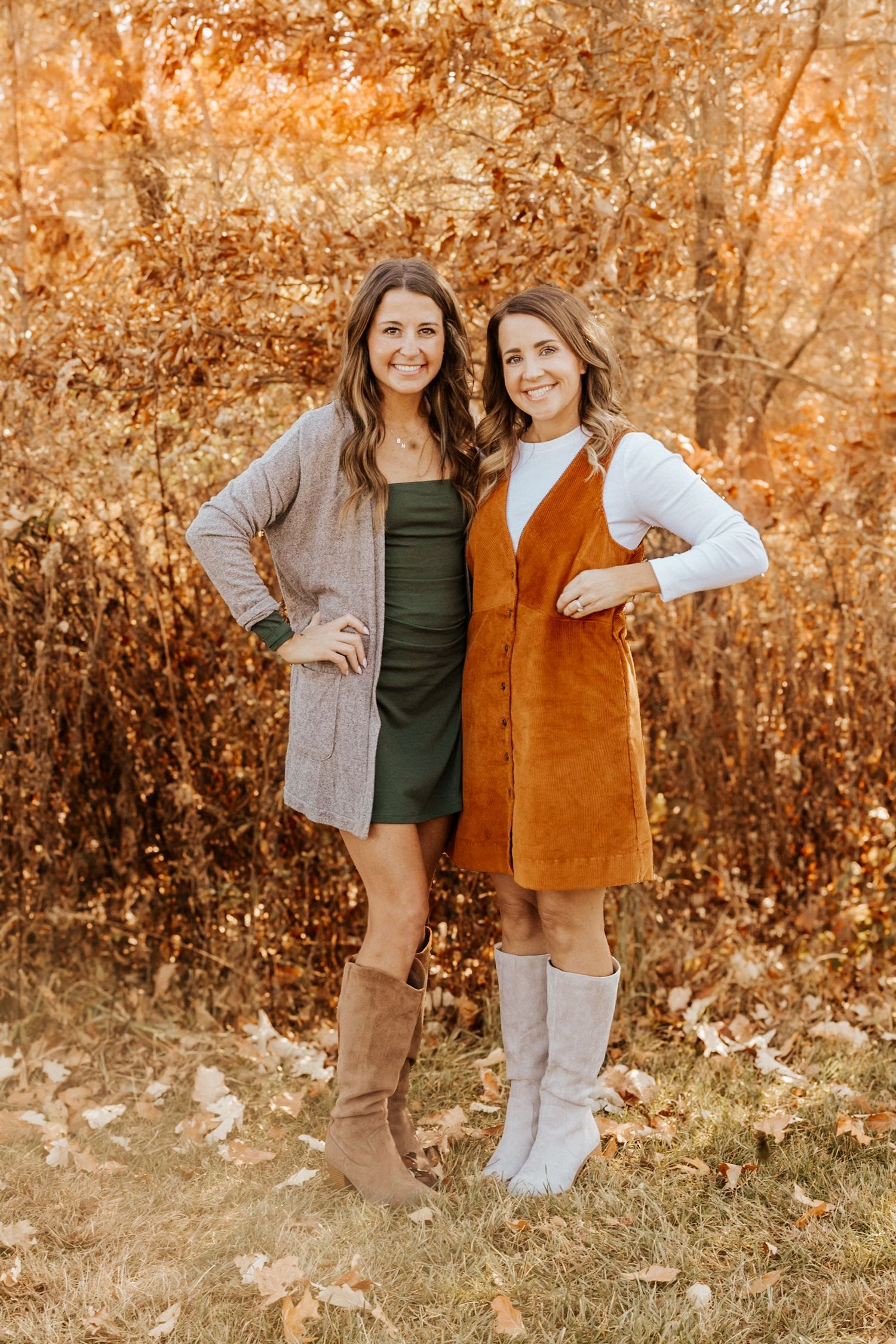 Two women in fall outfits pose outdoors among autumn foliage, wearing boots and layered dresses.