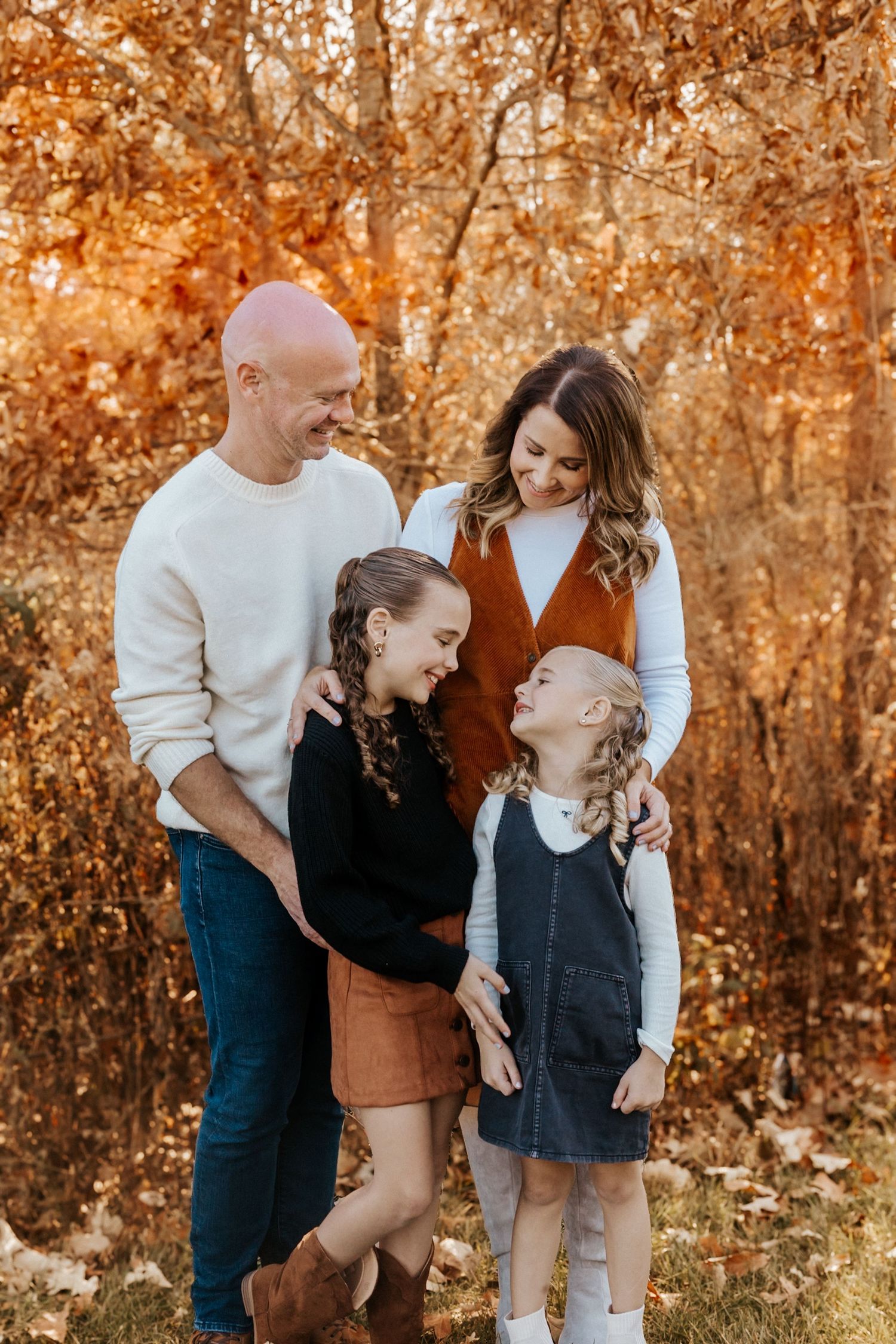 Family of four sharing a joyful moment outdoors among vibrant autumn foliage in coordinated fall outfits.