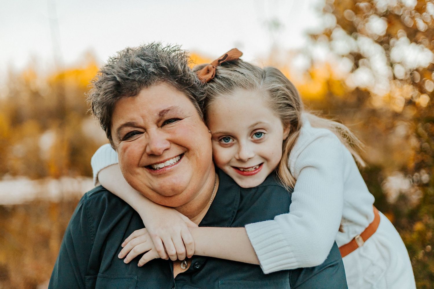 Smiling grandmother and granddaughter sharing a warm embrace outdoors during autumn season.