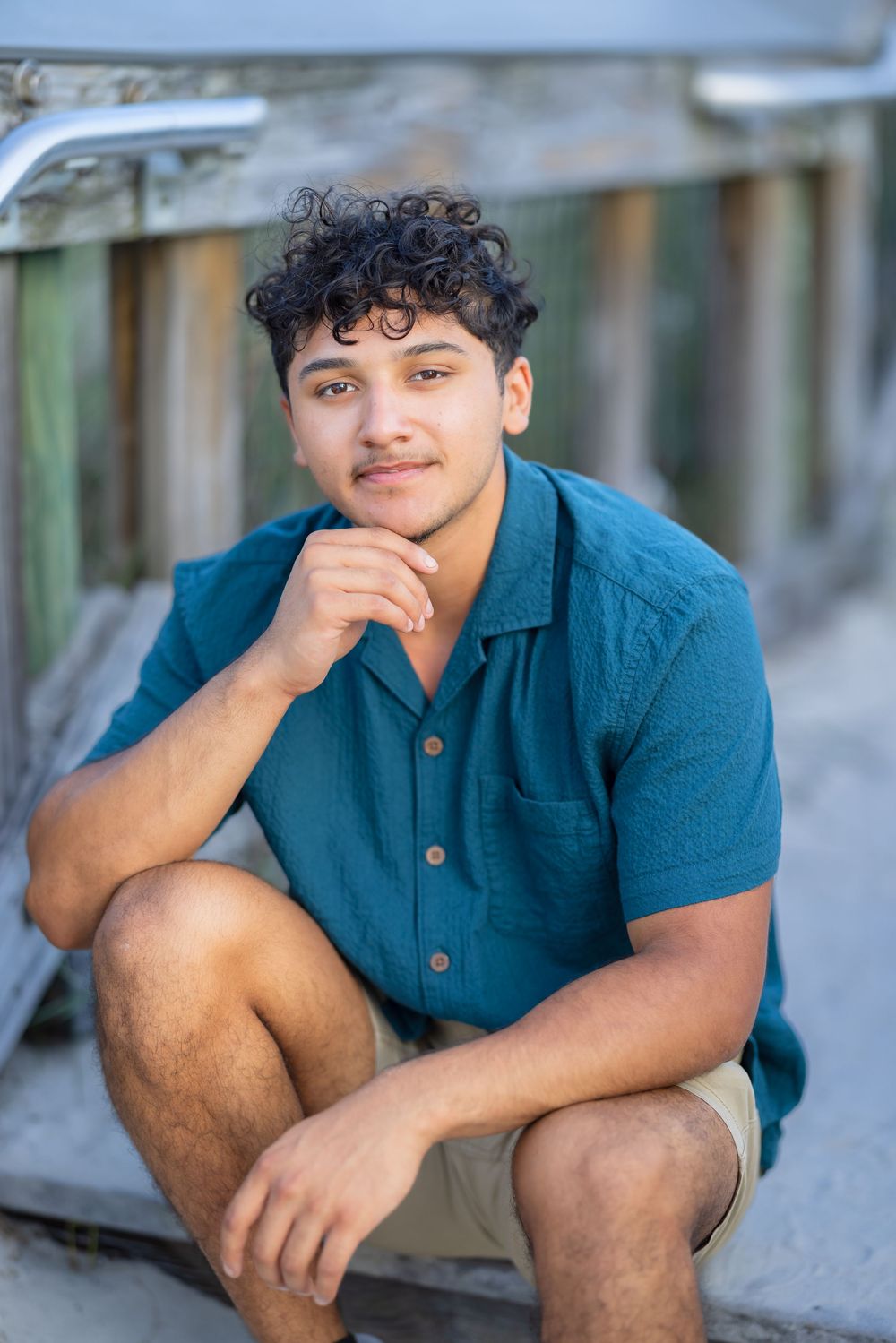 A person wearing a blue polo shirt sits casually outdoors while resting their hand near their face.