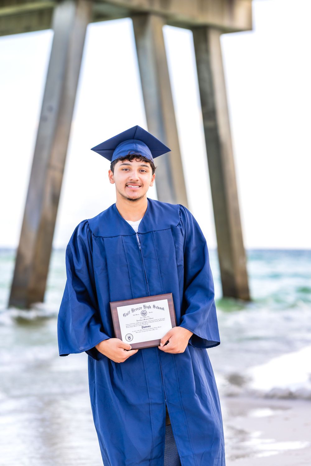 Graduate in blue cap and gown holding diploma stands near ocean pier in beachside graduation photo collage.