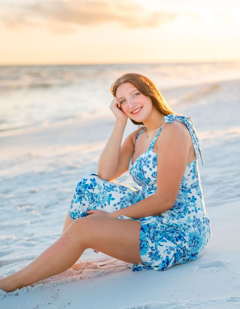 Someone wearing a blue and white floral swimsuit poses gracefully on a sandy beach at sunset.