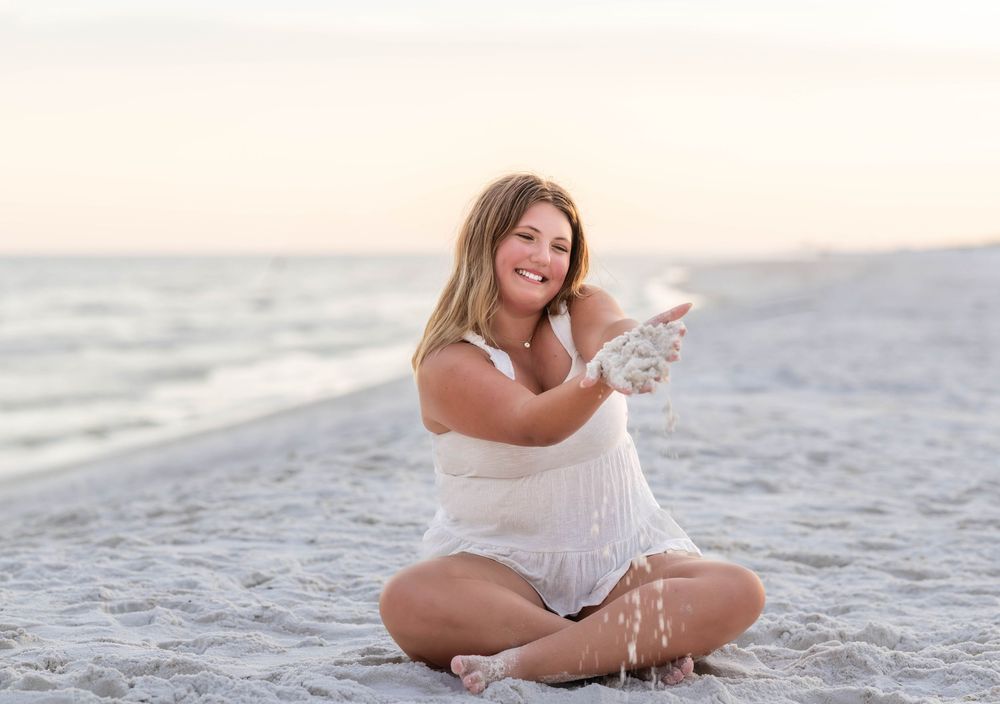 A person in white clothing poses on a sandy beach at sunset creating a serene coastal scene.