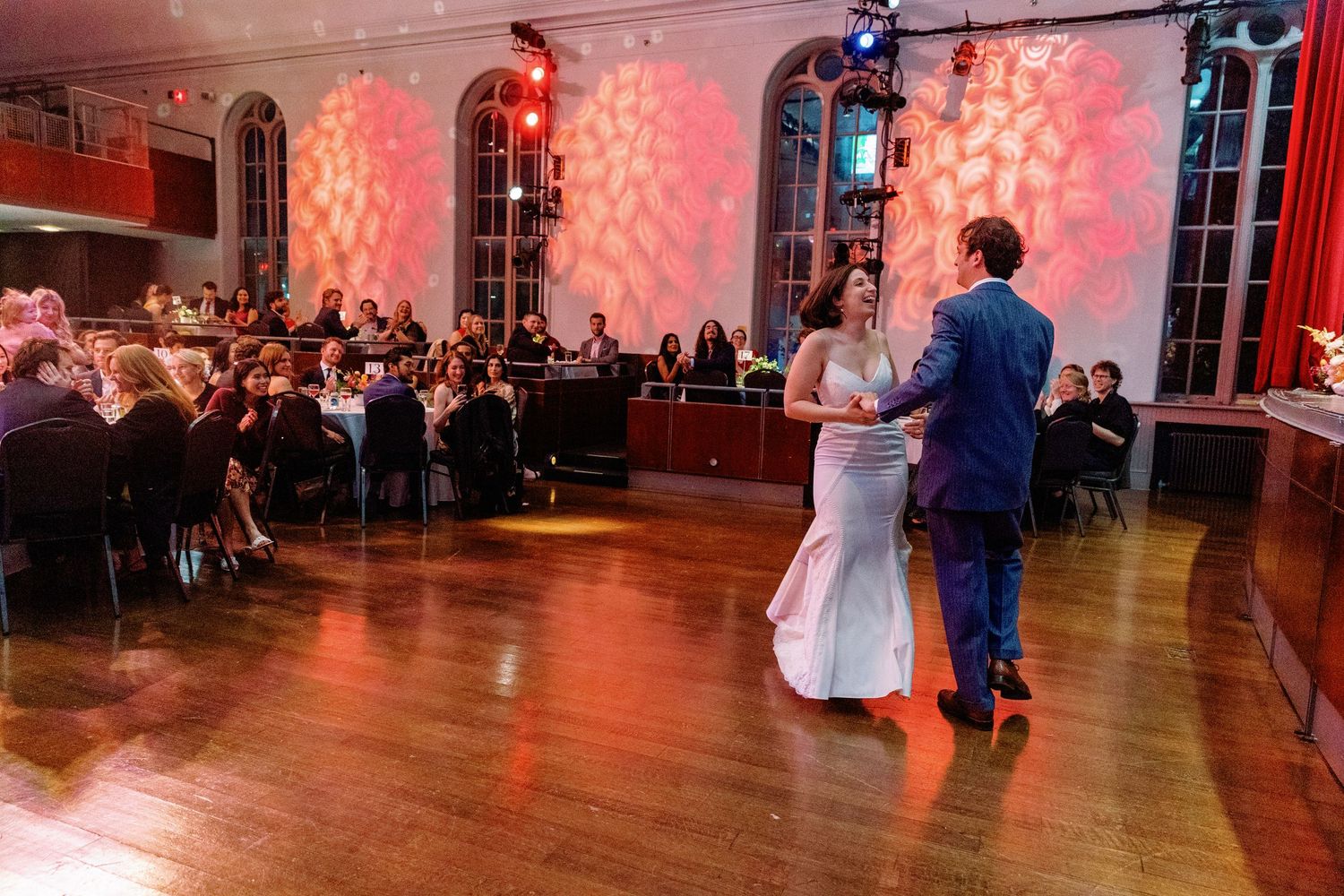 A wedding reception venue with a dance floor and guests dancing under warm red lighting and string lights.