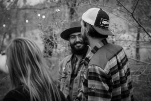Group of people conversing outdoors wearing casual attire and hats.