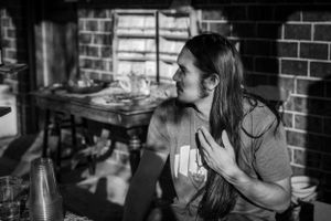 Black and white portrait of someone laughing while seated at a rustic indoor setting.