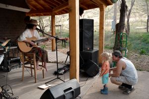 An acoustic performance on a covered porch with audience members watching.