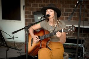 Musician performing with an acoustic guitar against a brick wall backdrop.