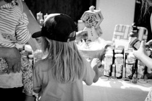 A black and white photo showing a person in a hat at a vendor booth or market display.