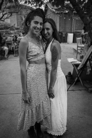Two friends in summer dresses sharing a joyful moment together at an outdoor gathering.