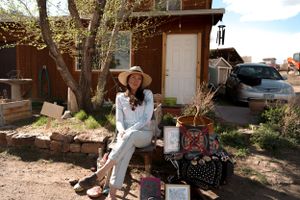 Person in white clothing and sun hat sitting on rustic porch with decorative items.