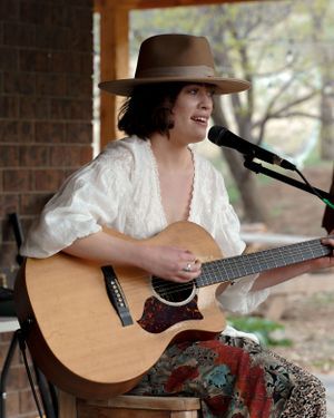 A musician in a brown hat plays acoustic guitar while performing on a covered outdoor stage.