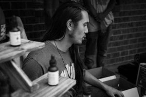 Person with long dark hair in profile sitting at a wooden table with bottles.