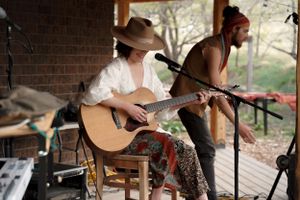 A performer plays guitar during an outdoor concert on a brick-walled porch.
