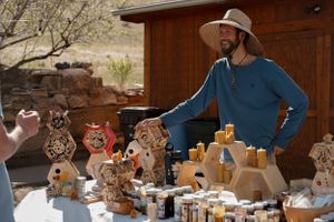 Vendor displays handmade wooden crafts at an outdoor market stand.