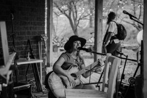 Musician playing acoustic guitar on stage at an outdoor venue in black and white photography.