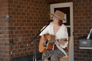Musician performing with acoustic guitar against brick wall background.