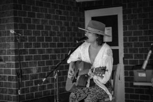 Black and white photo of acoustic guitar performance against brick wall.