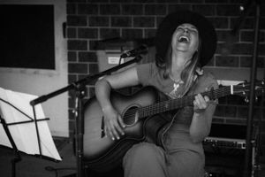 Musician passionately performing with an acoustic guitar against a brick wall background.