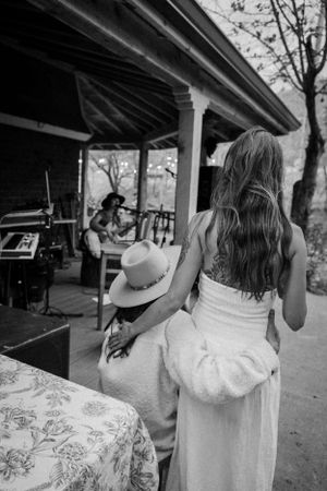 Black and white photo of a woman in a white dress watching musicians perform on a covered porch.