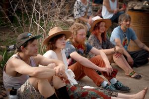 Group of people sitting casually outdoors wearing summer attire and hats.