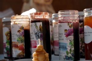 Colorful artisanal candles in glass jars with decorative labels displayed at market.