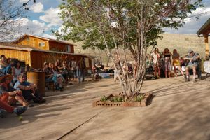 Rustic outdoor marketplace with wooden buildings and trees in a desert setting.