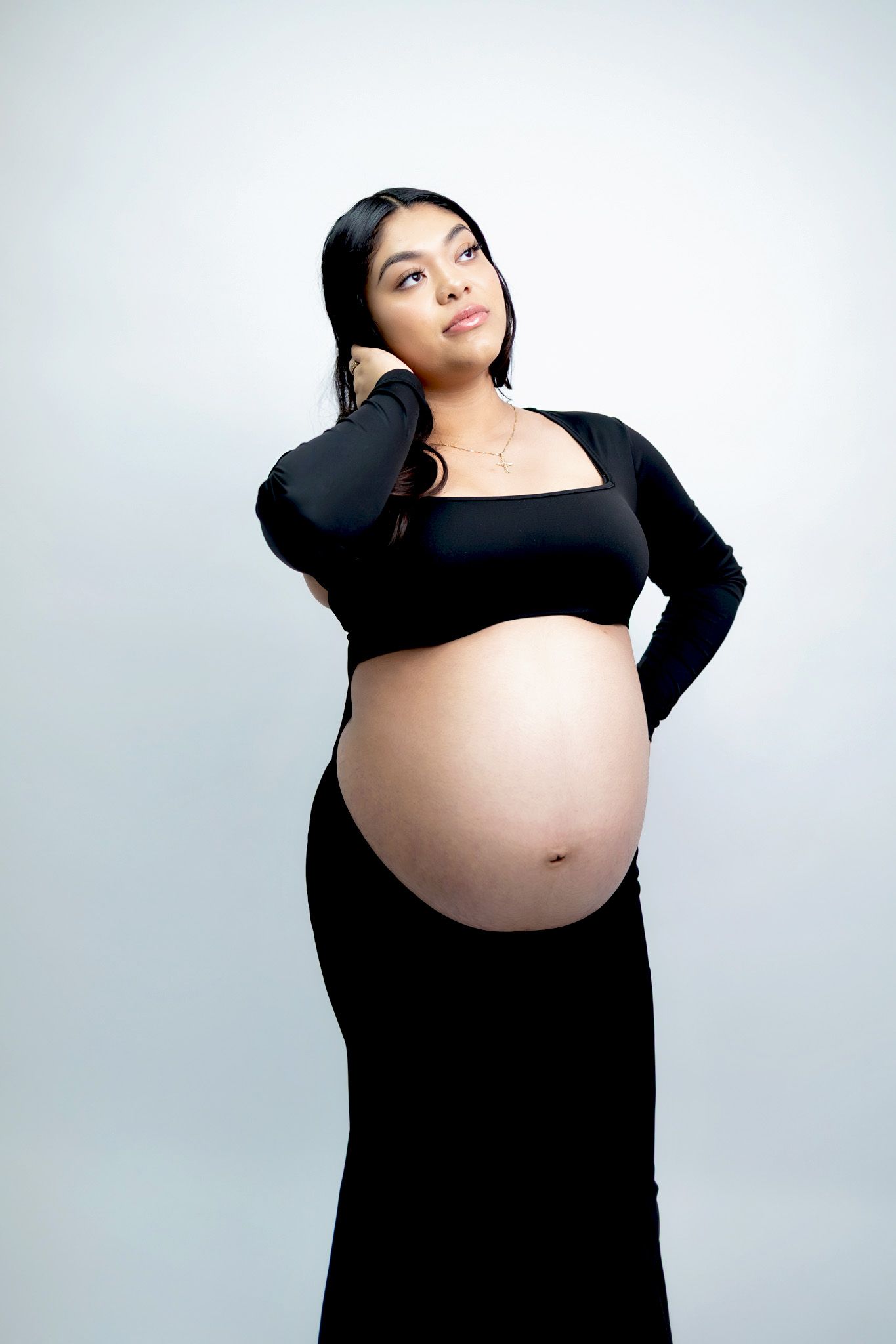 Four artistic black and white maternity photos show an expectant person in various poses wearing black clothing against a light backdrop.