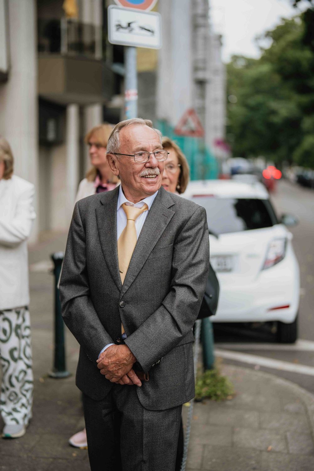 Well-dressed senior gentleman smiles warmly on city street.