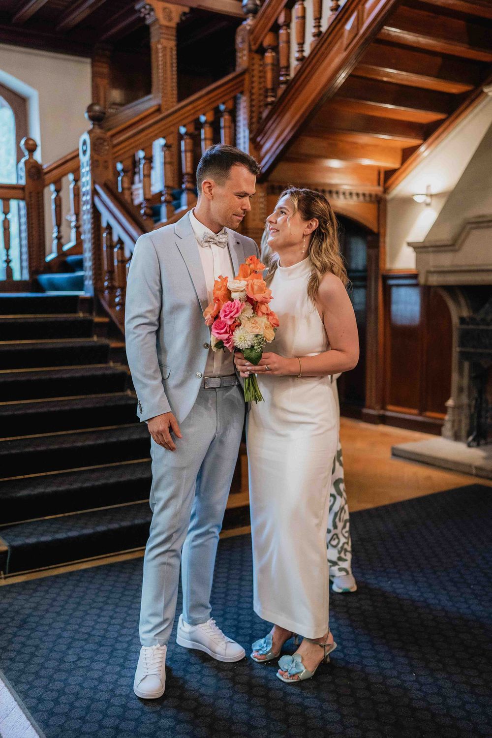 Newlyweds share intimate moment on wooden staircase with bouquet.