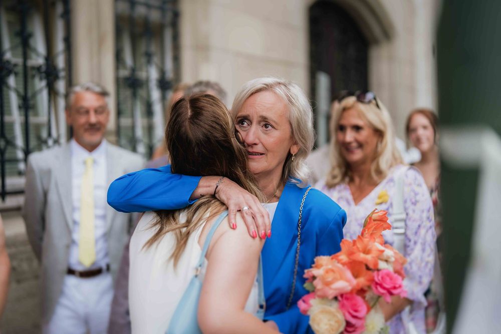 Wedding guests share warm embraces and emotional moments during outdoor celebration with colorful bouquet.