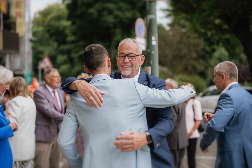 Wedding guests exchange heartfelt hugs during outdoor celebration gathering.