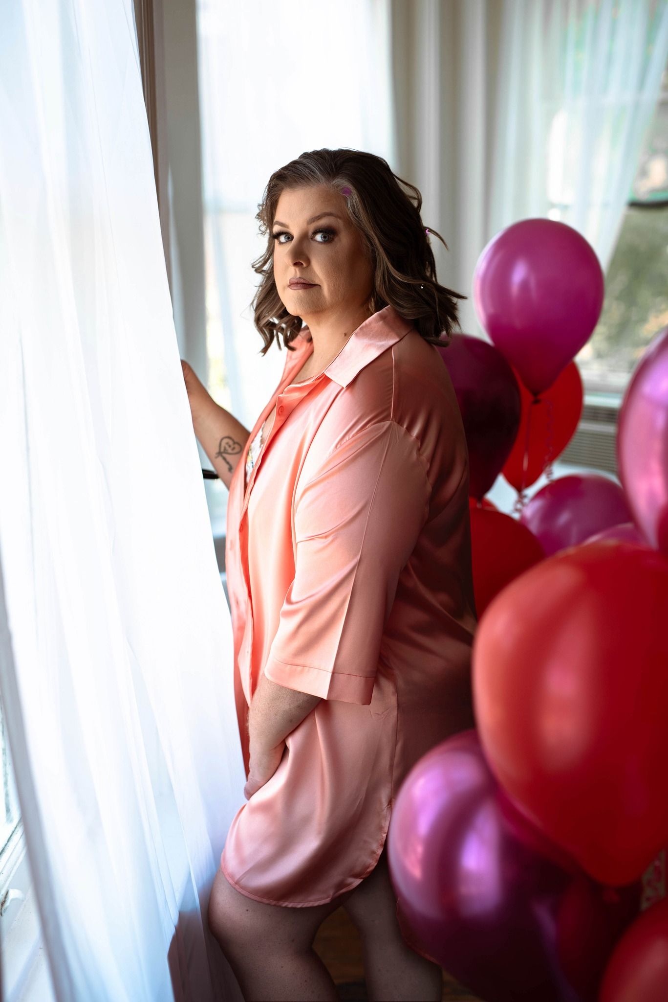 A beautiful 53 year old woman poses in front of a window with balloons in the background celebrating her birthday with a boudoir session