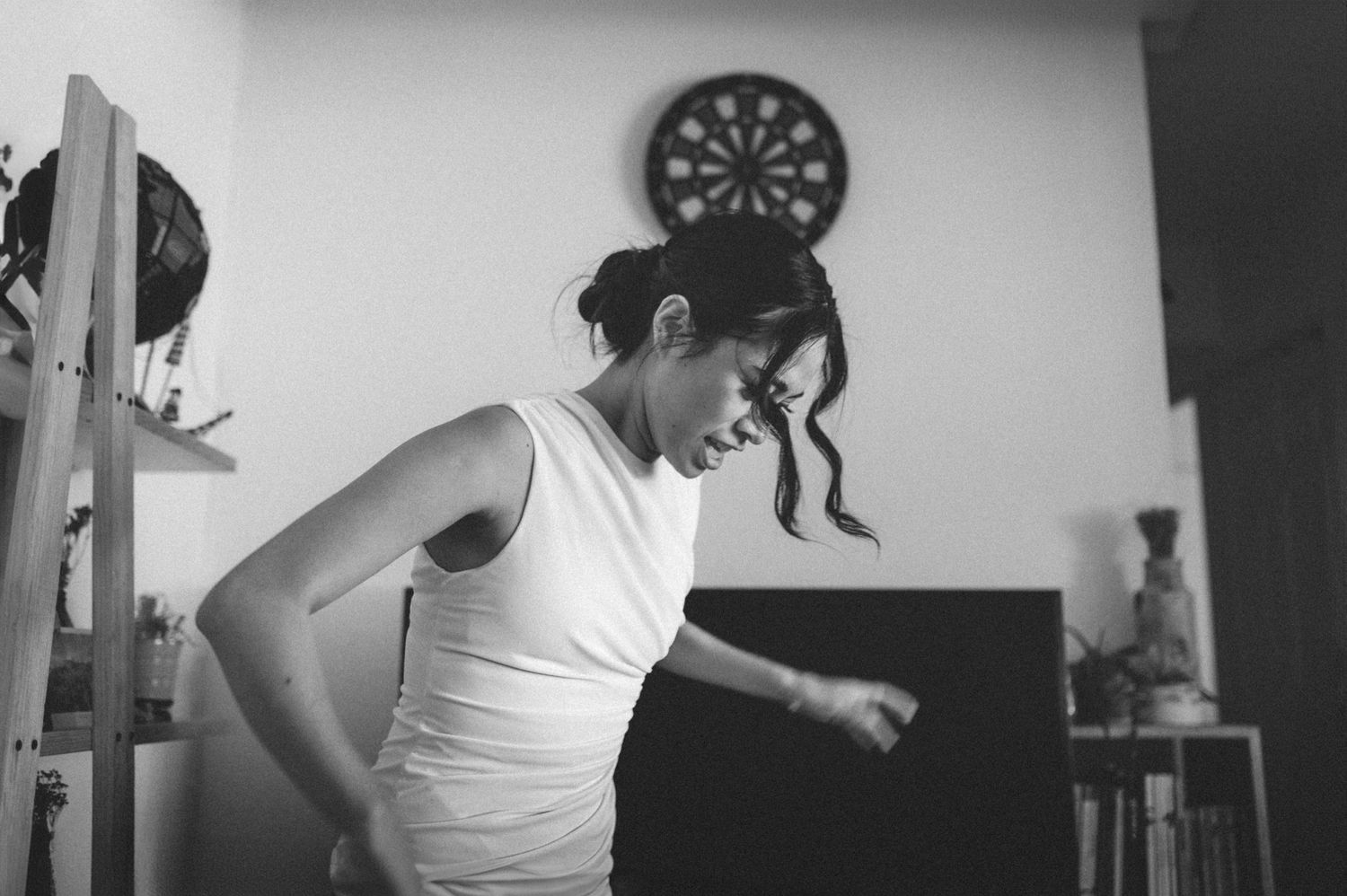 Black and white photo of someone playing darts on a dart board in a casual indoor setting.