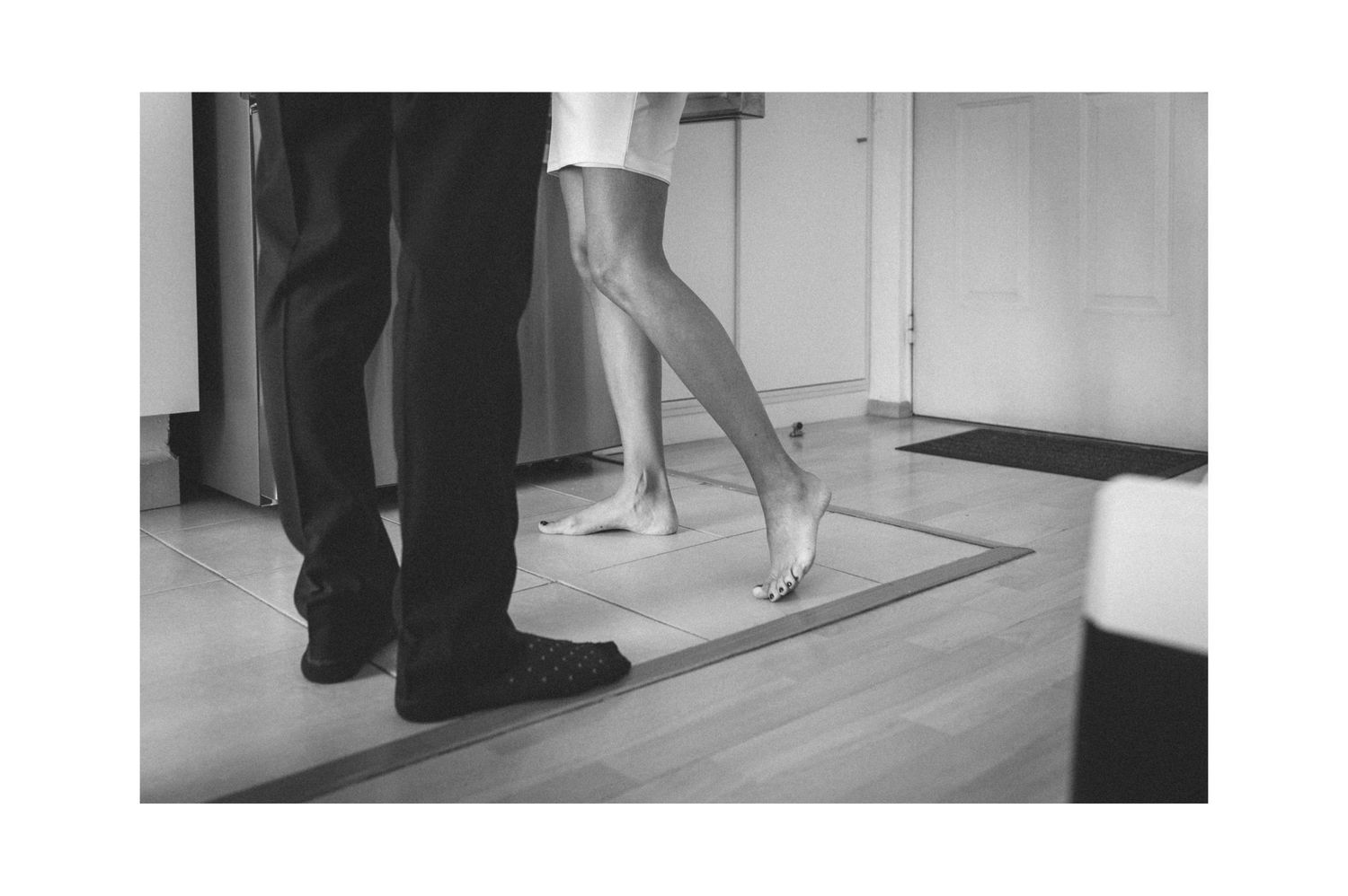 Black and white photo of two pairs of feet dancing on a hardwood floor.