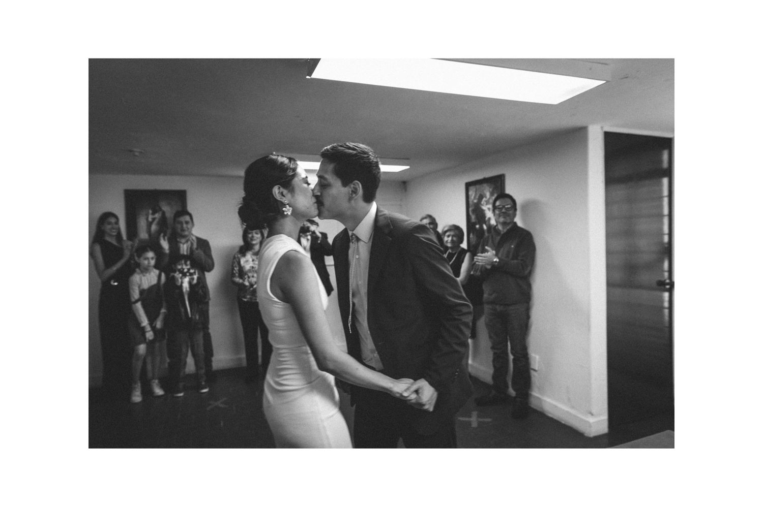A black and white photo capturing a dance in an indoor space with onlookers.